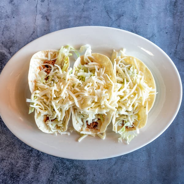 Three El Cabo Restaurant tacos filled with meat, shredded lettuce, and cheese on a white plate.