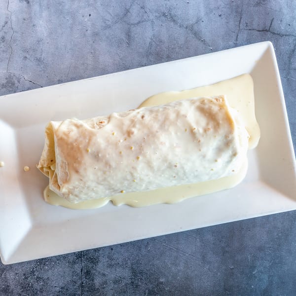 A large burrito covered in white cheese sauce, served on a white rectangular plate.