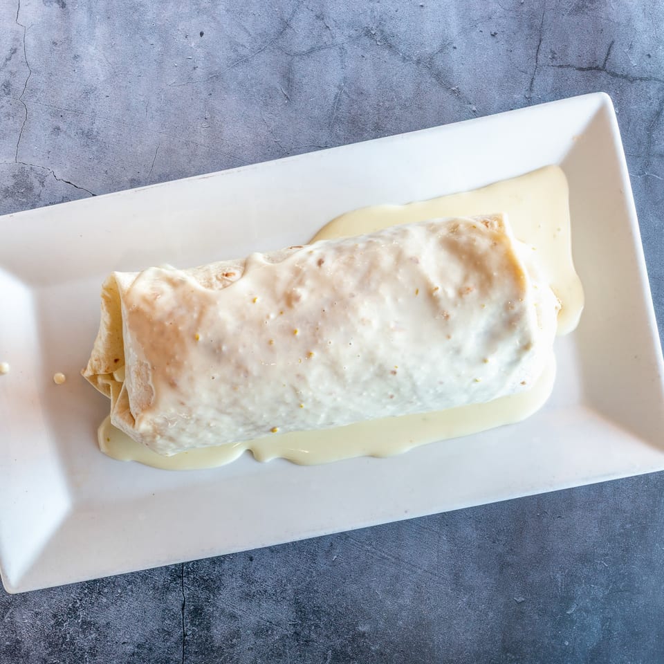 A large burrito covered in white cheese sauce, served on a white rectangular plate.
