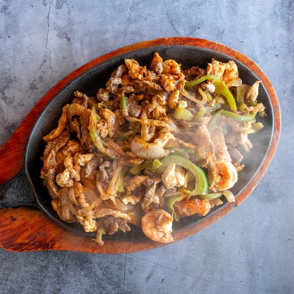 Sizzling fajitas with steak, chicken, shrimp, onions, and green peppers on a cast iron skillet.